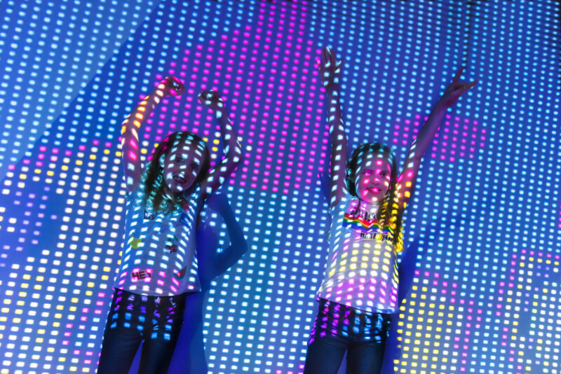 Digital Dimensions at Eureka! Two smiling children with their arms in the air with digital dimensions projected lights across them